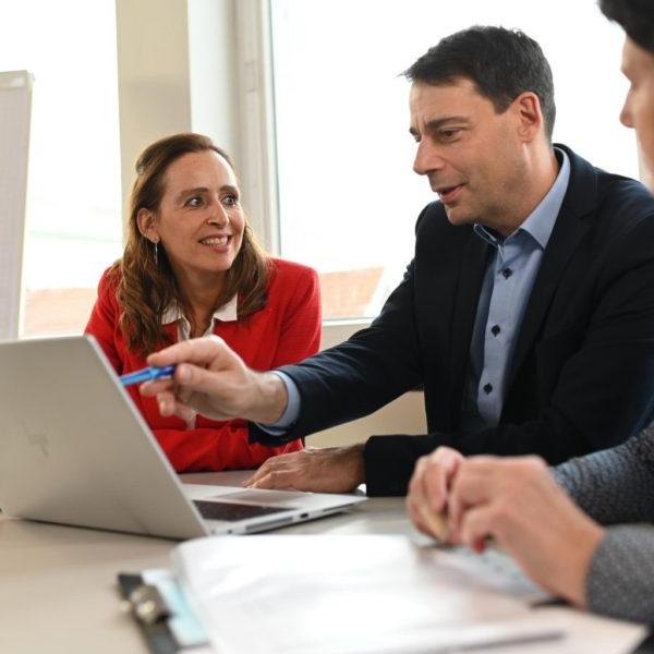 Two men looking at a laptop and talking with a woman